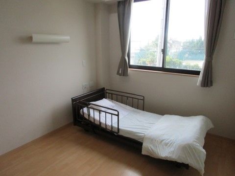 フローリングで小さな窓と手すり付きベッドのある一人用居室