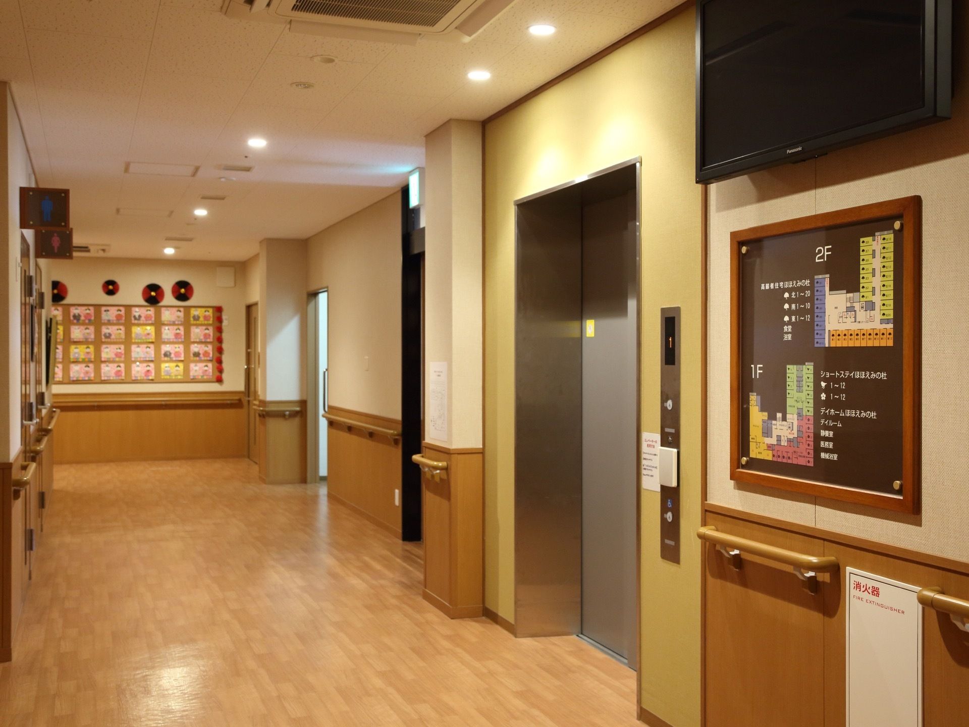 壁に建物の案内板が掛けられている。通路の壁には、手すりが設置されている。エレベーターやトイレなどがある。