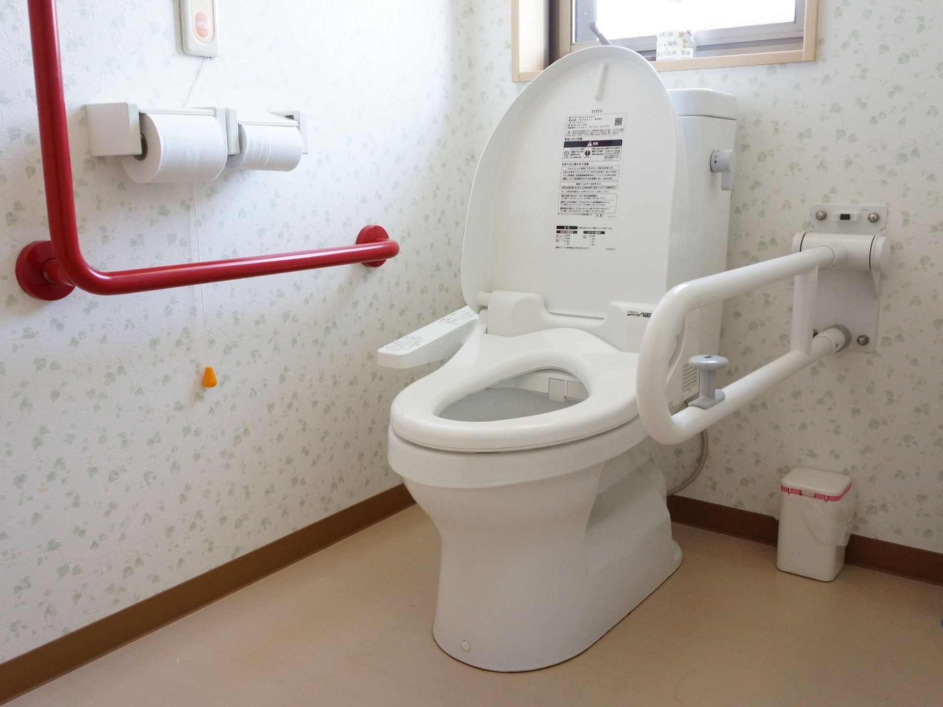白くきれいに磨かれた便器を備えたトイレであり、周囲は模様の描かれた壁で覆われている。便器の両側には手すりやつかまり用の棒が配備されている。