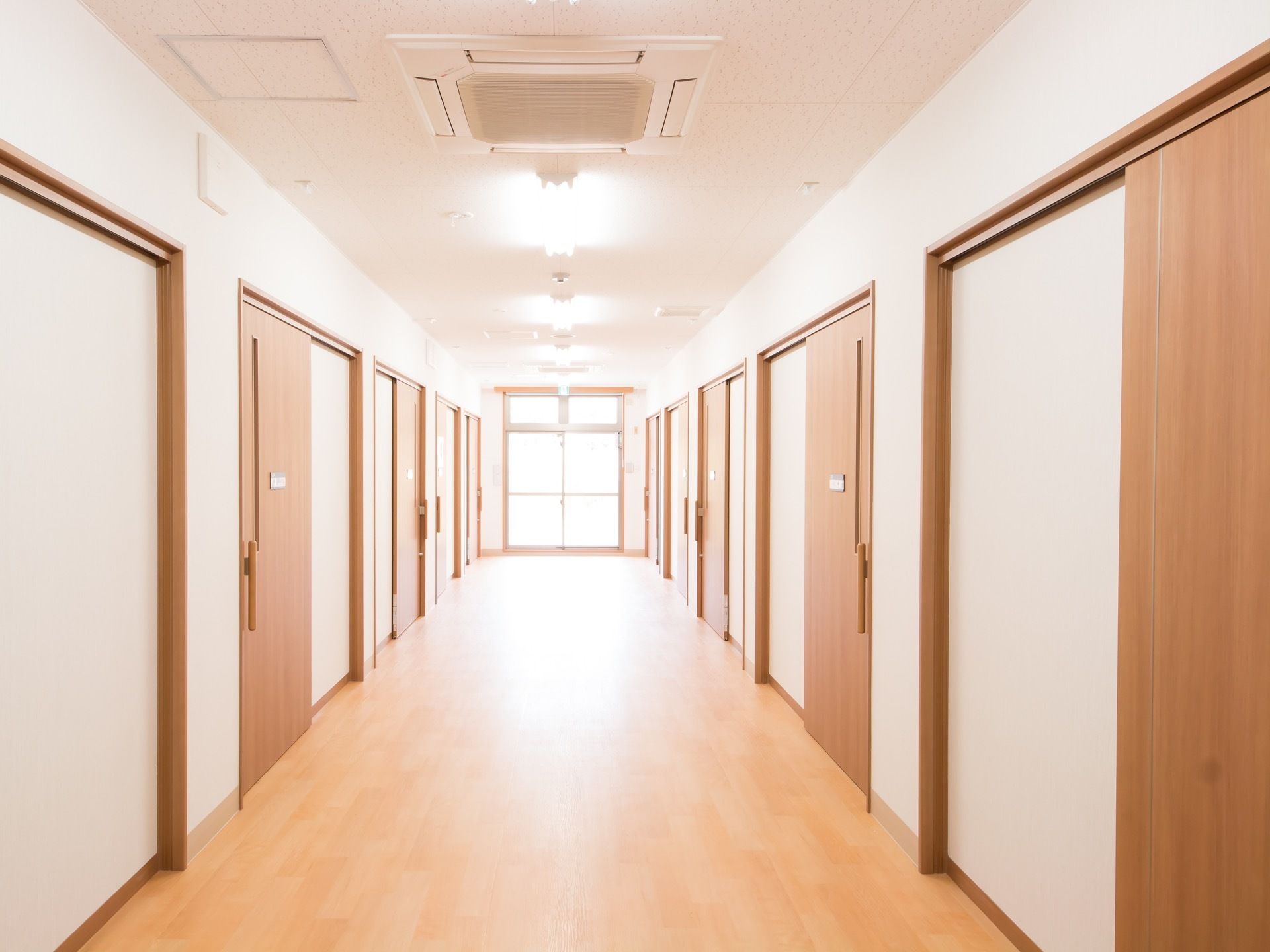 広々とした明るい廊下である。居室の扉が両サイドに並んでいる。突き当りには、日差しが差しこむ窓が設けられている。