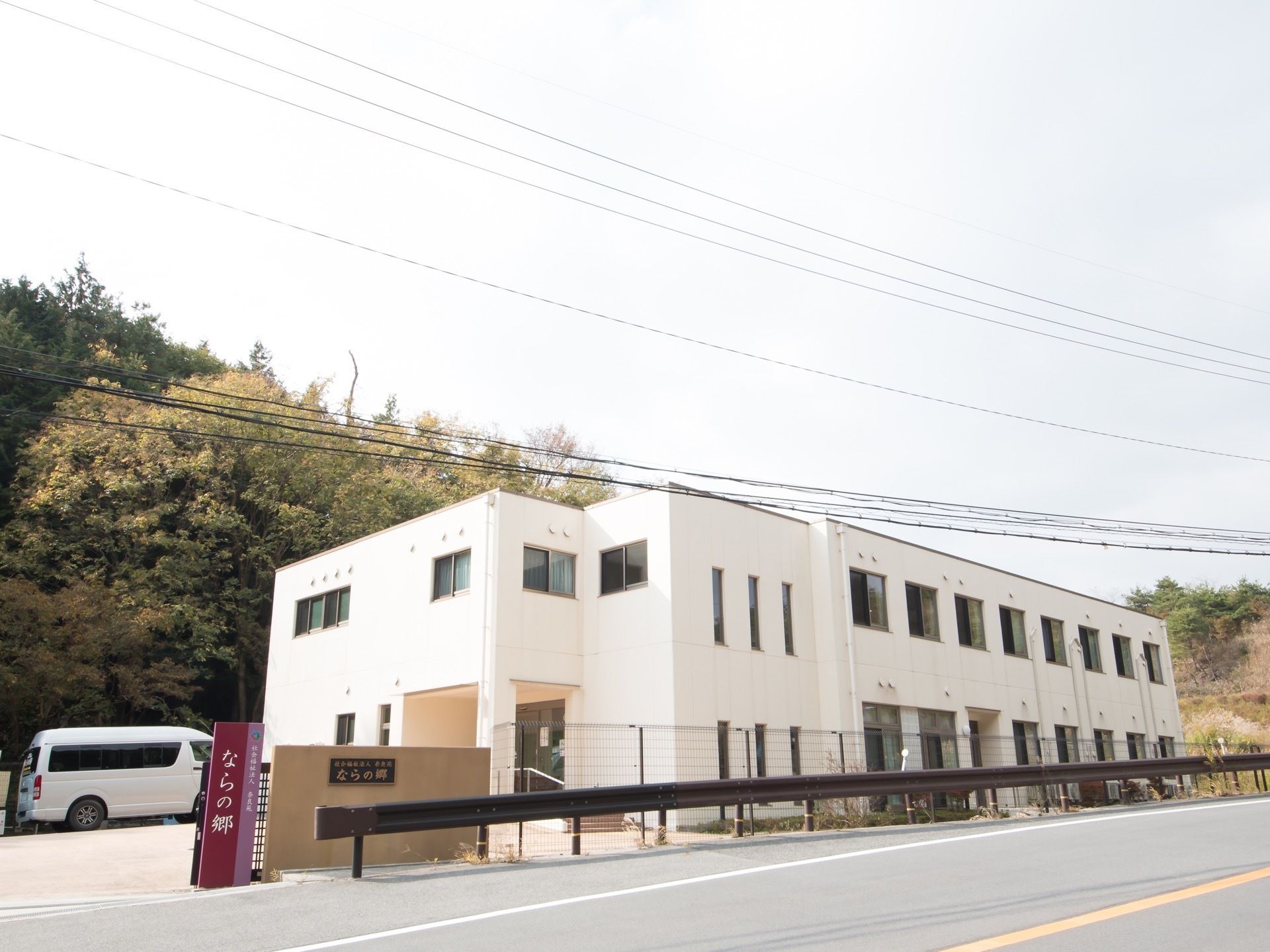 自然豊かな環境の中に建つ白い２階建ての施設である。駐車場が建物前に設けられている。敷地はフェンスで囲まれている。