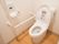 居室に完備されたトイレである。温水洗浄便座が設置されており、白いＬ型手すり、呼び出しボタンが壁に取りつけられている。