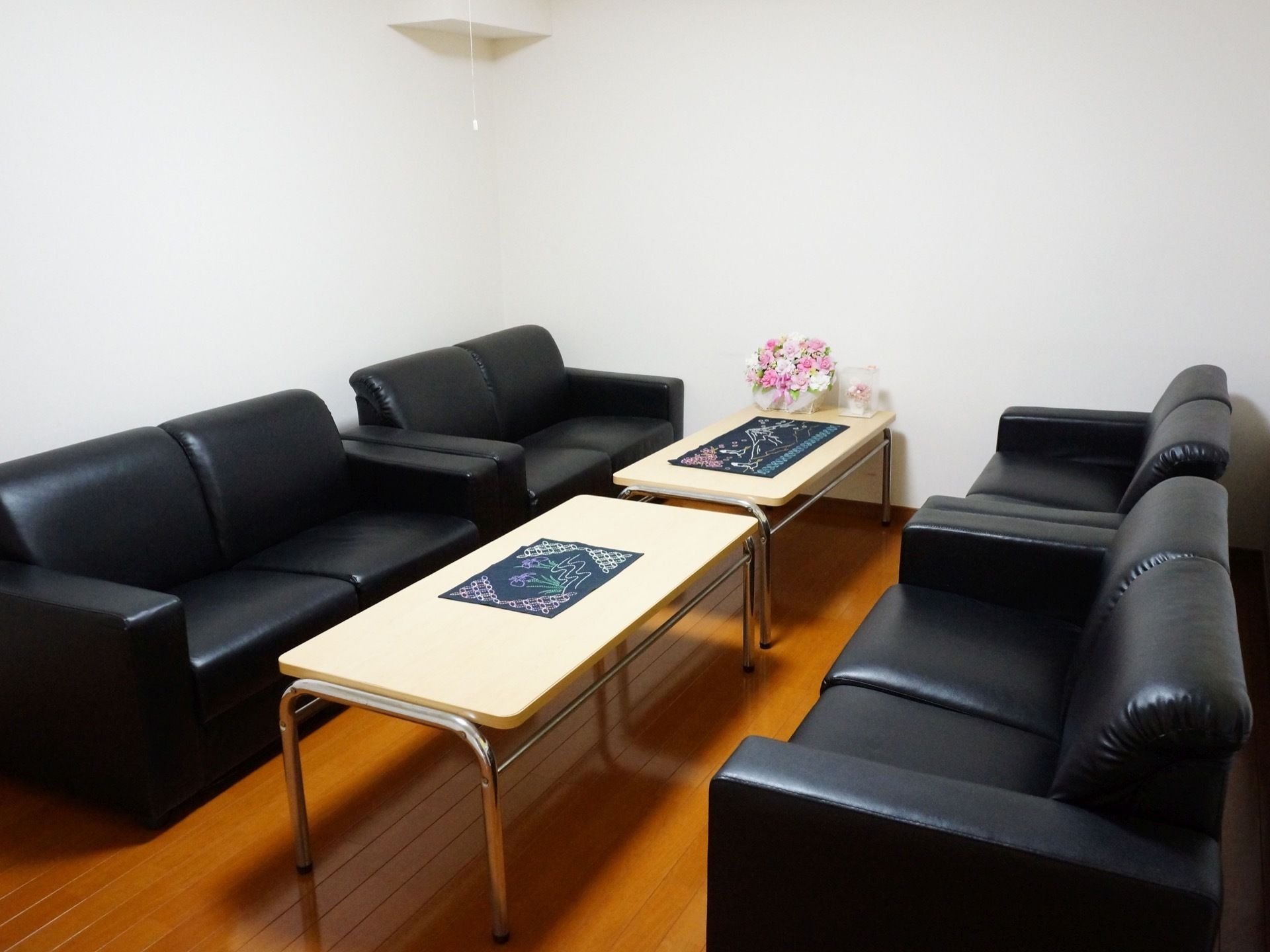 二人掛けのソファが4台置いてある。中央にはテーブルが2台並んでいる。テーブルの上には花が飾られている。