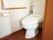 清潔感のある白と温かみのある茶色で統一された内装の室内には、タンク付きのトイレが1つとトイレットペーパー掛けが設置されている。