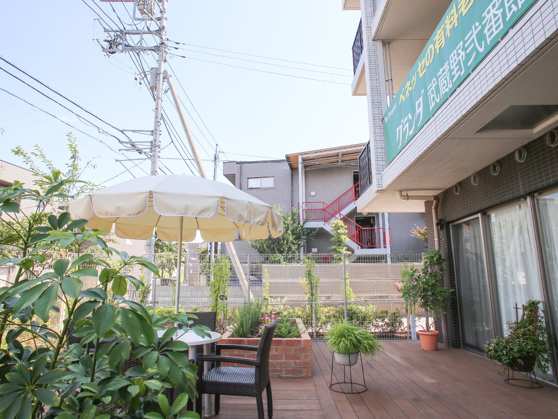 1階に取り入れた食堂から出入り可能なウッドデッキのテラス。観葉植物や花壇、パラソル付きのガーデンセットがある。
