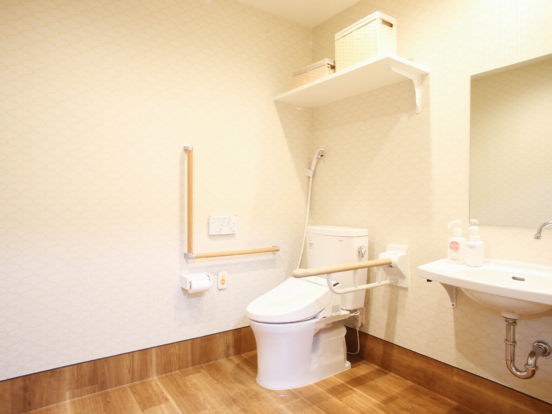 ゆったりとした空間にトイレと洗面台を置いたフローリングのトイレスペース。安全面に考慮した手すりやさっと掃除できるシャワーも完備。