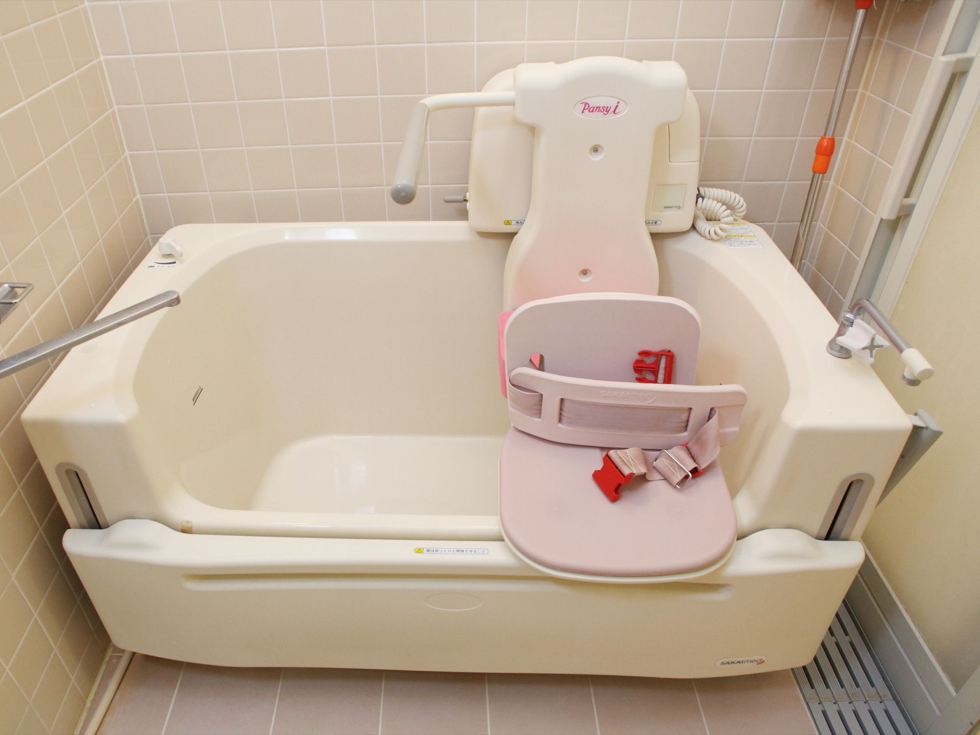 浴槽には椅子が付属しており、ベルトが付いている。壁や床はタイル張りになっていて、全体的に明るく、きれいな浴室になっている。