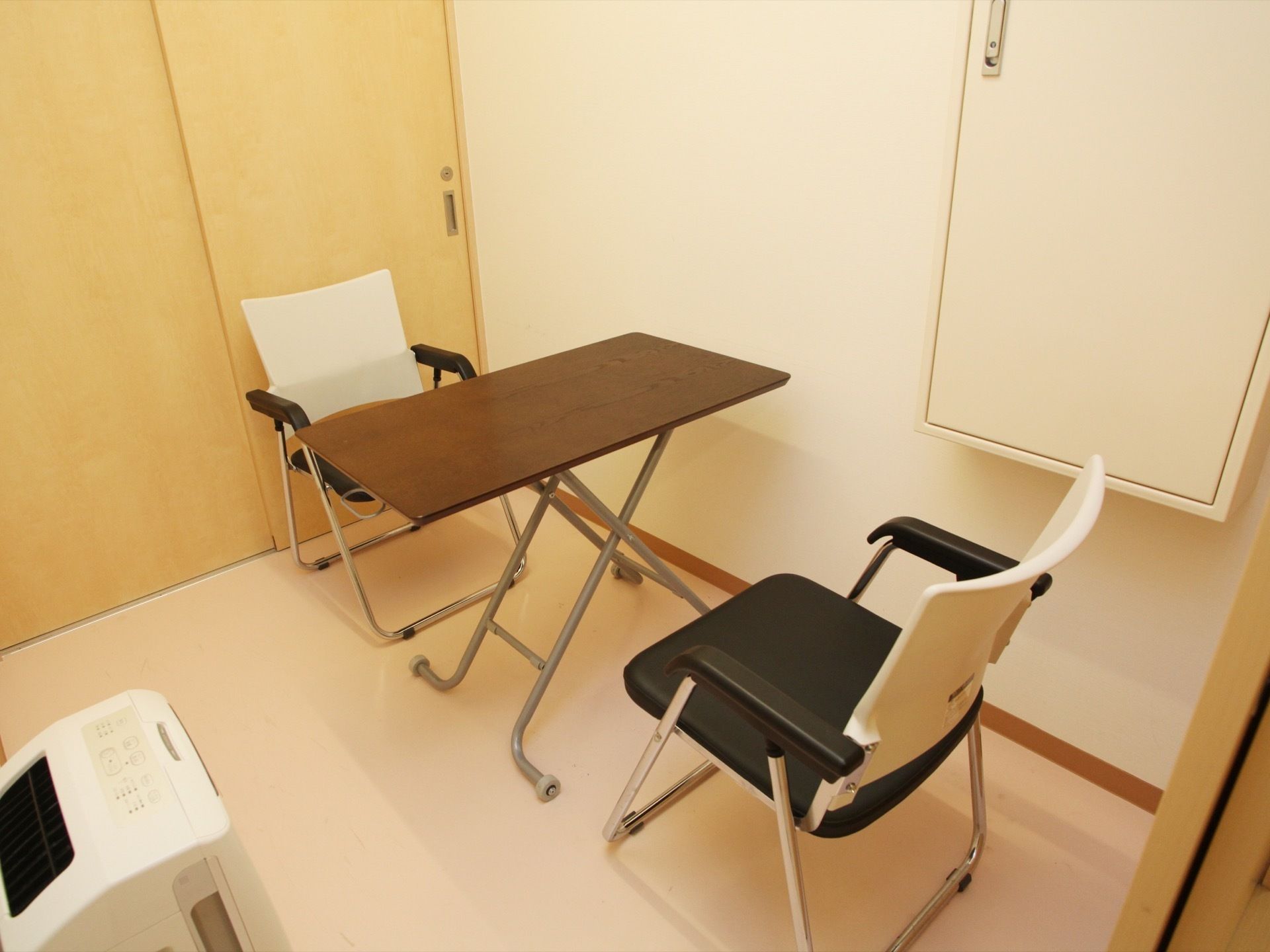 相談室にはテーブルと、向かい合って椅子が設置されている。扉は引き戸になっている。空気清浄機が置かれてある。