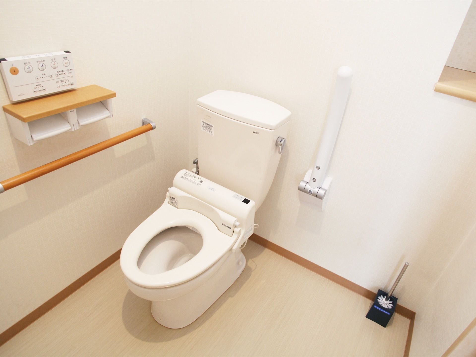 白い内装のトイレは、掃除が行き届き清潔感がある。中は広めで、木製の手すりとトイレットペーパーホルダーが付いている。