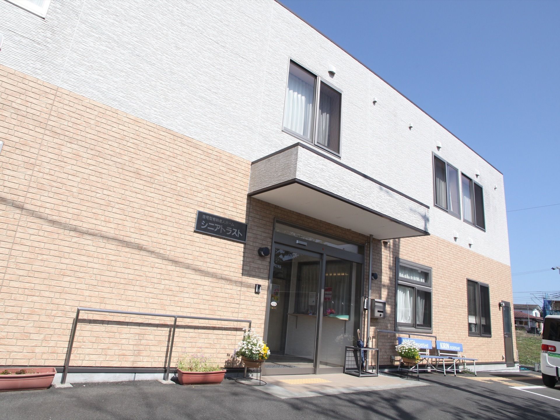 二階建ての建物に窓が数か所ある。玄関付近には花や傘立て、ベンチが設置されている。入口は自動ドアになっている。