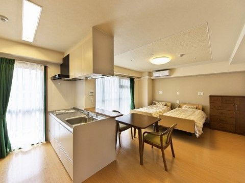 窓が２つあるワイドスパンの部屋で、窓と平行にベッドが2台並んでいる。台所があり、レンジフードと吊り棚収納がある。