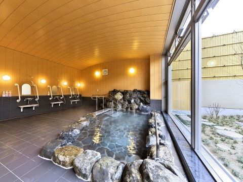 ガラス越しに坪庭を眺められる大きな岩風呂は手すりが付いている。広い洗い場を挟んで、シャワー台が３つ並んでいる。