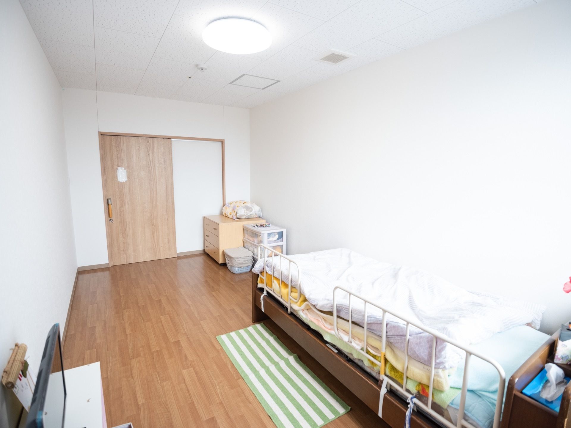 木目調タイプのフローリング部屋である。壁側にサイドガードが設置された、ベッドが設置されている。向かい側にはテレビがある。