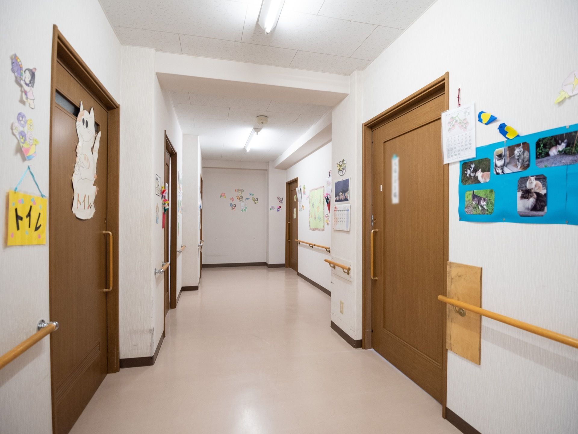 明るい色合いの通路である。建具は落ち着いた茶系に施されている。両側には、手すりがある。
