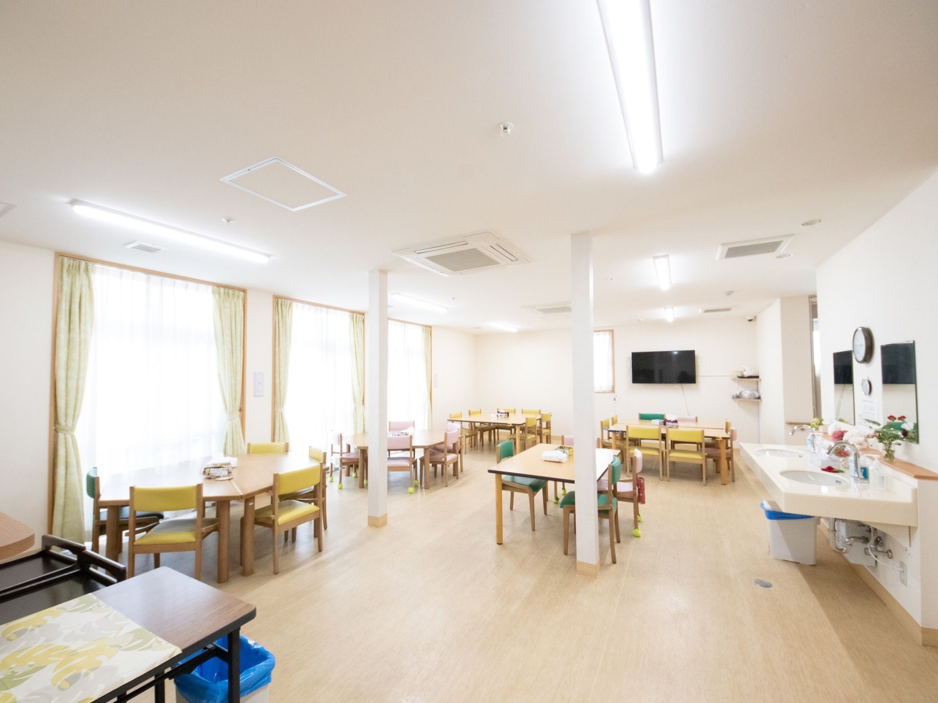 白木調の床を取り入れた共有スペースである。横側はガラス戸が並び、ゆったりと間隔をおいてテーブルセットを並べている。