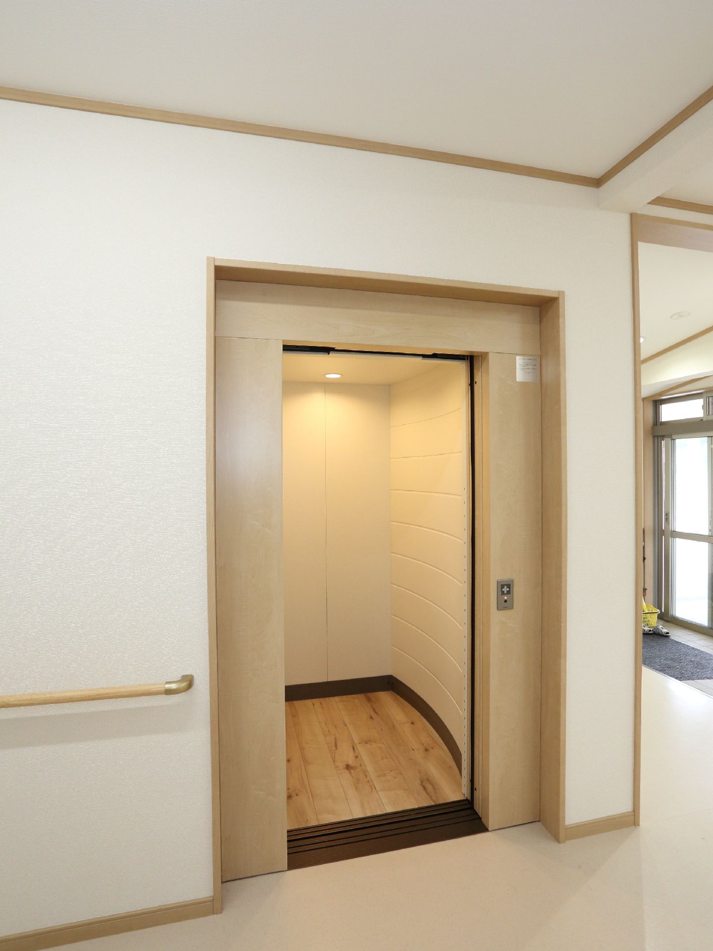 玄関を入ってすぐのところに、エレベーターがある。床は明るい色のフローリングになっている。壁はクリーム色で統一されている。