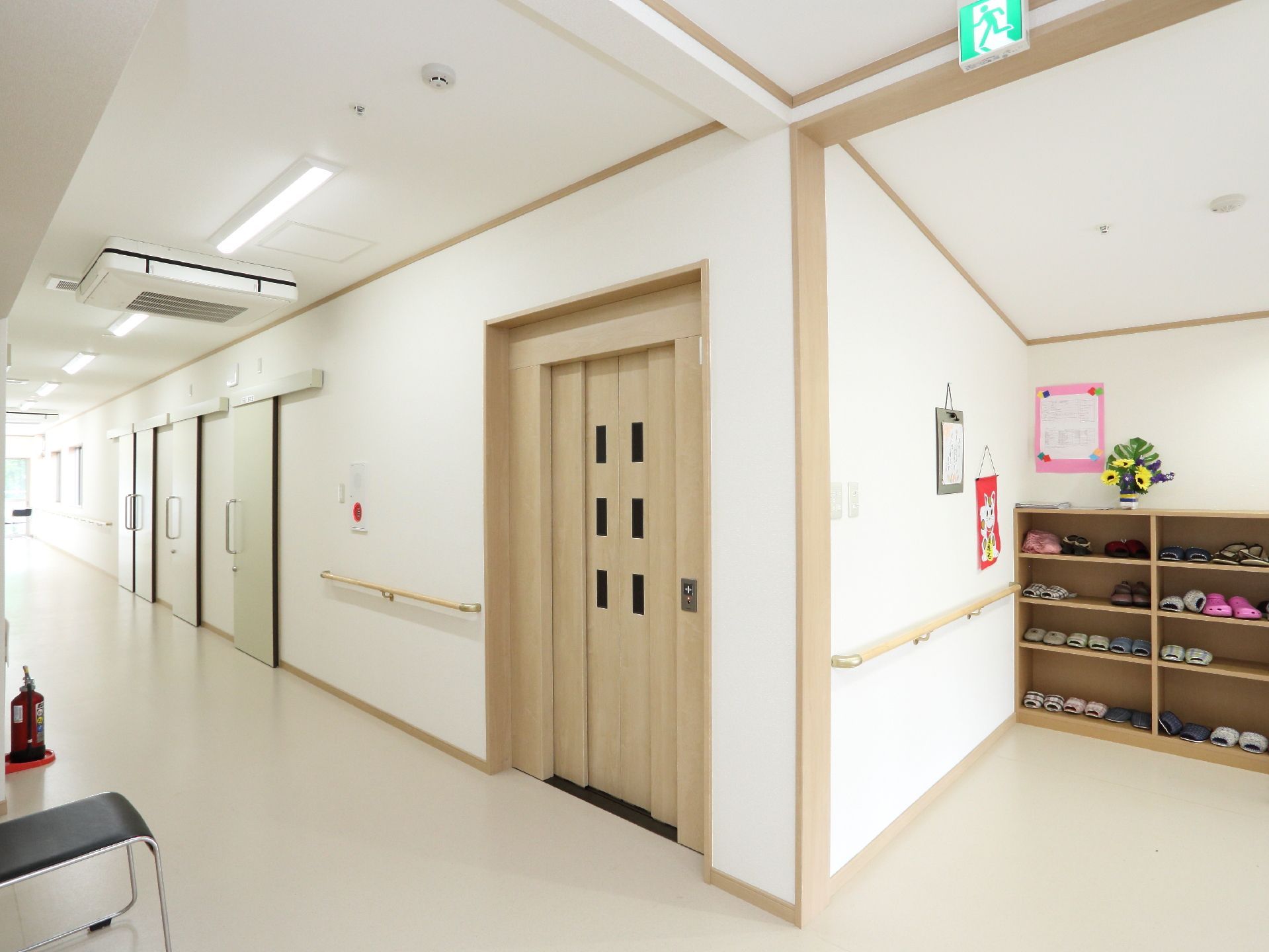 白い床はきれいに磨き上げられている。靴箱にスリッパが並べられている。壁には手すりがある。白と明るい茶色で統一されていて、明るい内部である。