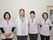 施設の廊下をバックに4名のスタッフが笑顔で立っているのが写っている。全員女性でピンクの制服を着用している。年齢層は幅広い。