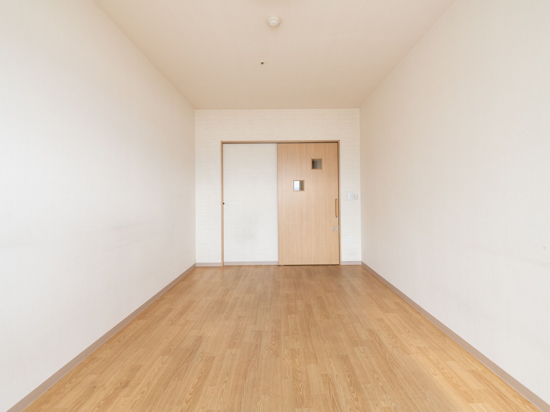 フローリングの床と白い壁で、明るくナチュラルな雰囲気の居室である。部屋のドアは引き戸式になっている。