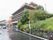 5階建ての建物で、施設までの通路の右側には石垣があり、上には草木が生えている。建物の正面に駐車場があり、数台の車が止められている。