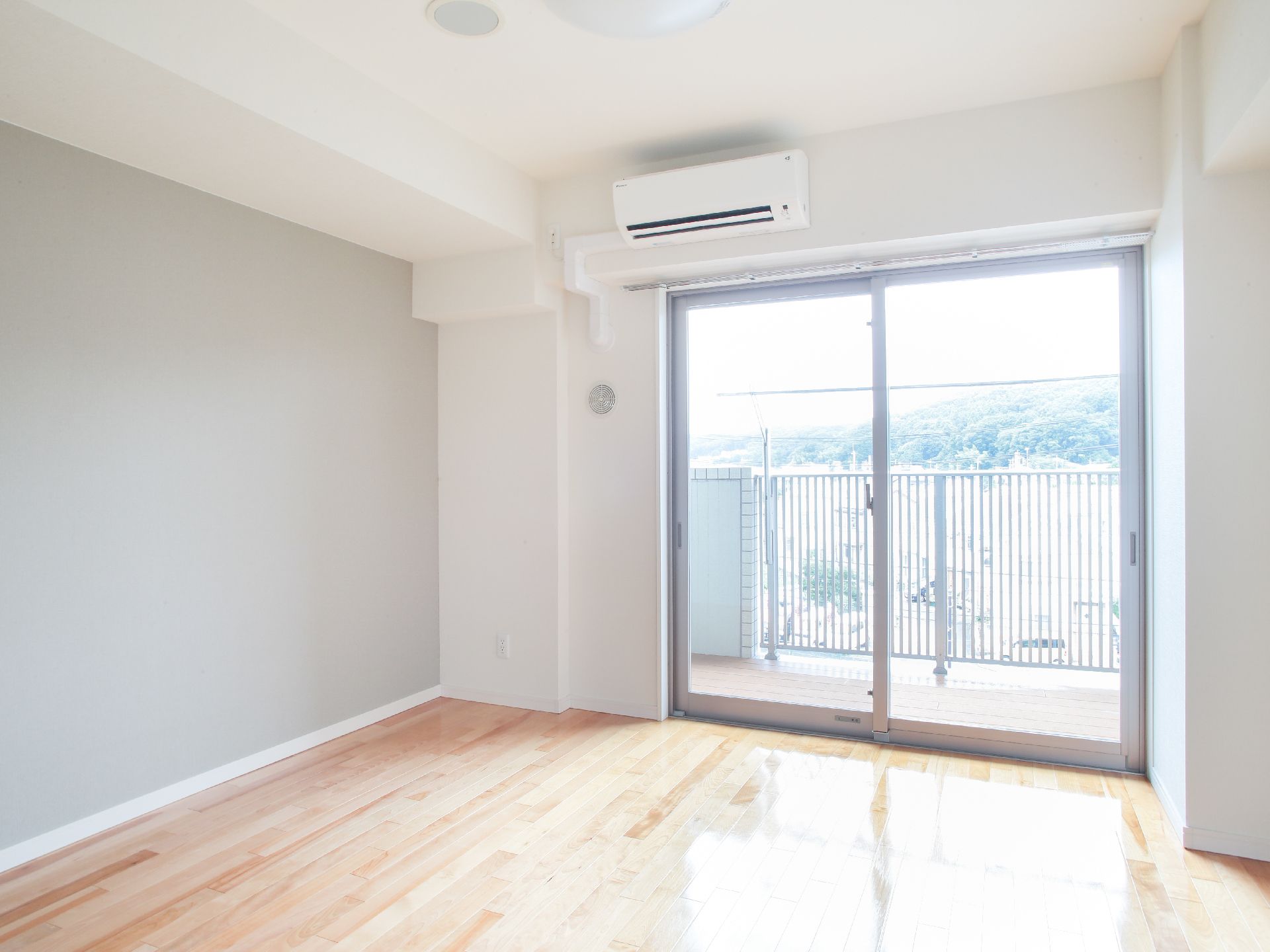 窓が大きく明るい部屋で、ベランダからは遠くの自然を楽しめる。エアコンが取り付けられており、快適に過ごすことができる。