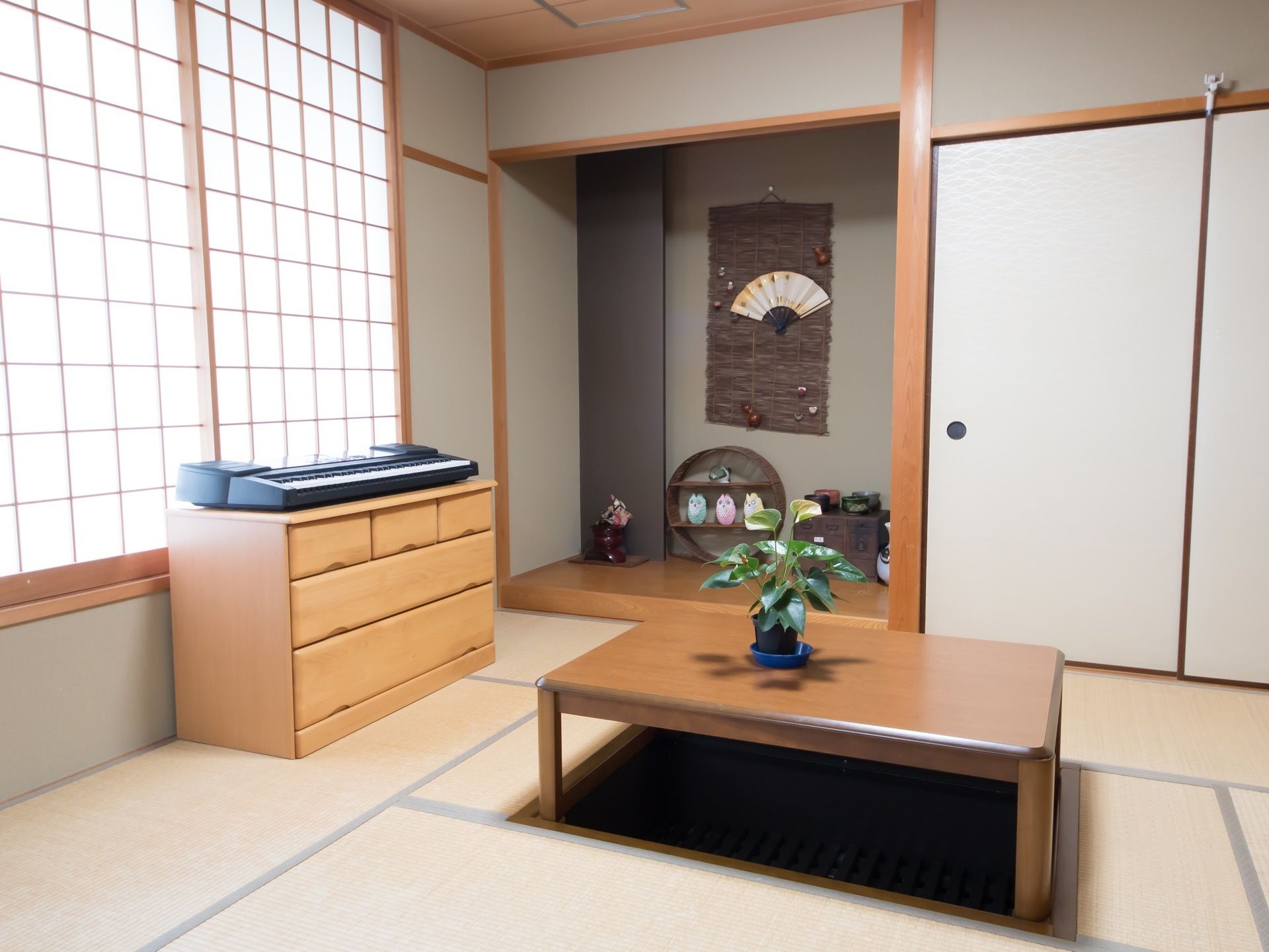 畳の部屋には、掘りごたつがあり、床の間には置物や扇子が飾ってある。引き出しタンスの上にはキーボードが置いてある。