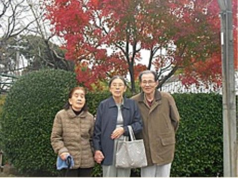 紅葉した木と緑の生垣を背景に並んでいる三人の入居者