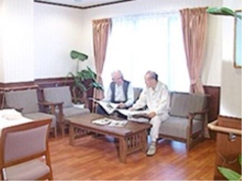 共有スペースに腰かけ、新聞を読みながら会話している入居者二人