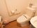 居室に備わった洋式トイレである。壁にはＬ字型の手すりと呼出ボタンが備わっている。入口側には洗面台も設置されている。
