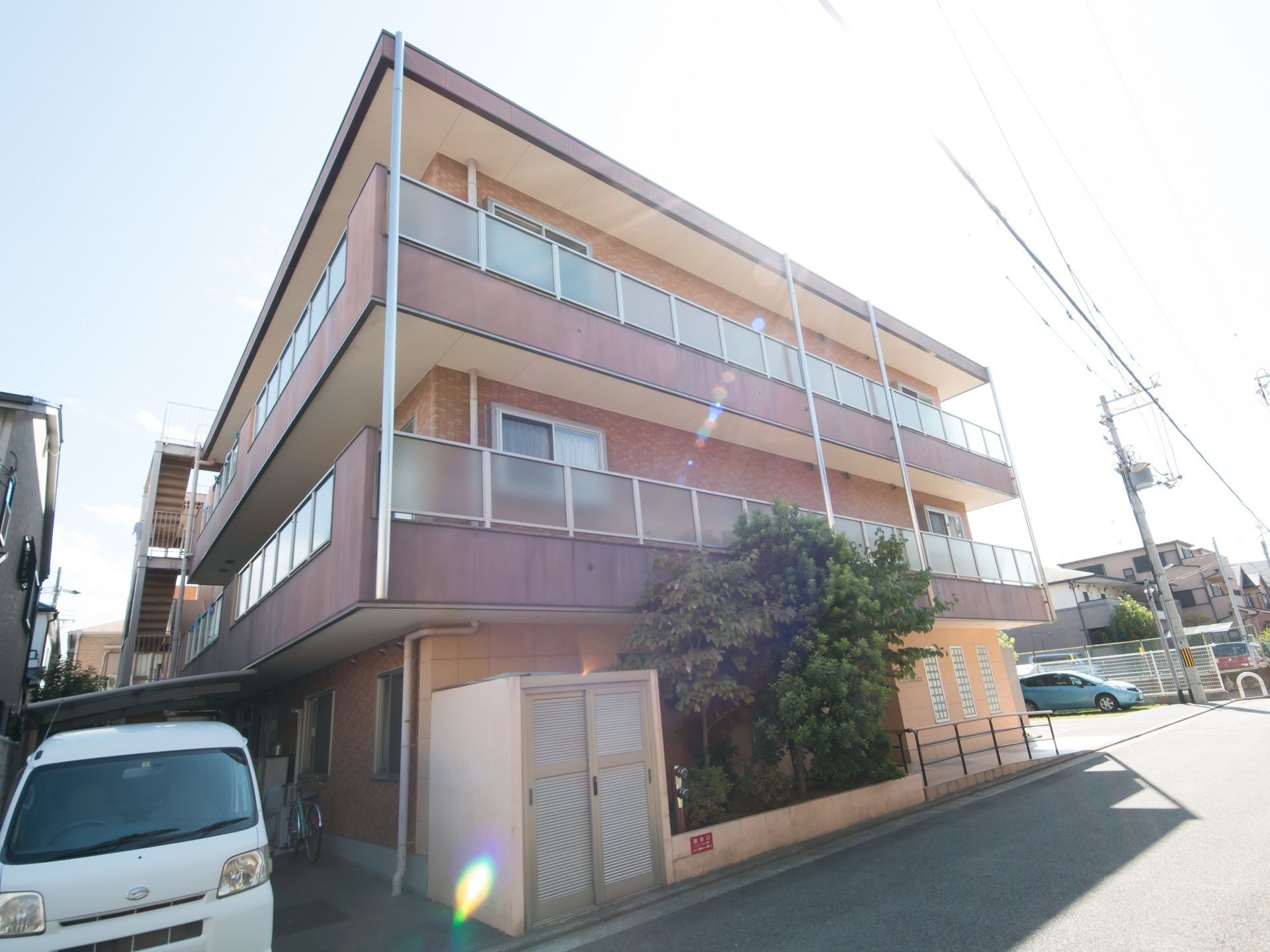 施設建物の出入口の横には植え込みがあり、樹木が植えられている。２階と３階にはベランダが設置されている。