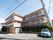落ち着いた色調の３階建ての施設である。居室にはすりガラス板で目隠しされたバルコニーがある。玄関の脇には駐車スペースがある。