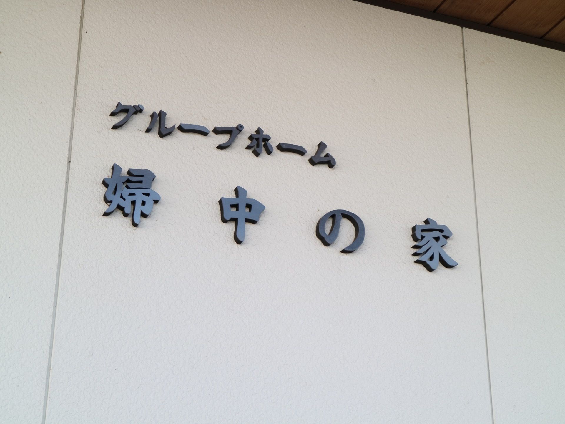 せり出した屋根の下に白い壁に施設名が取り付けられている。黒くて大きな見やすい文字で２行書かれている。