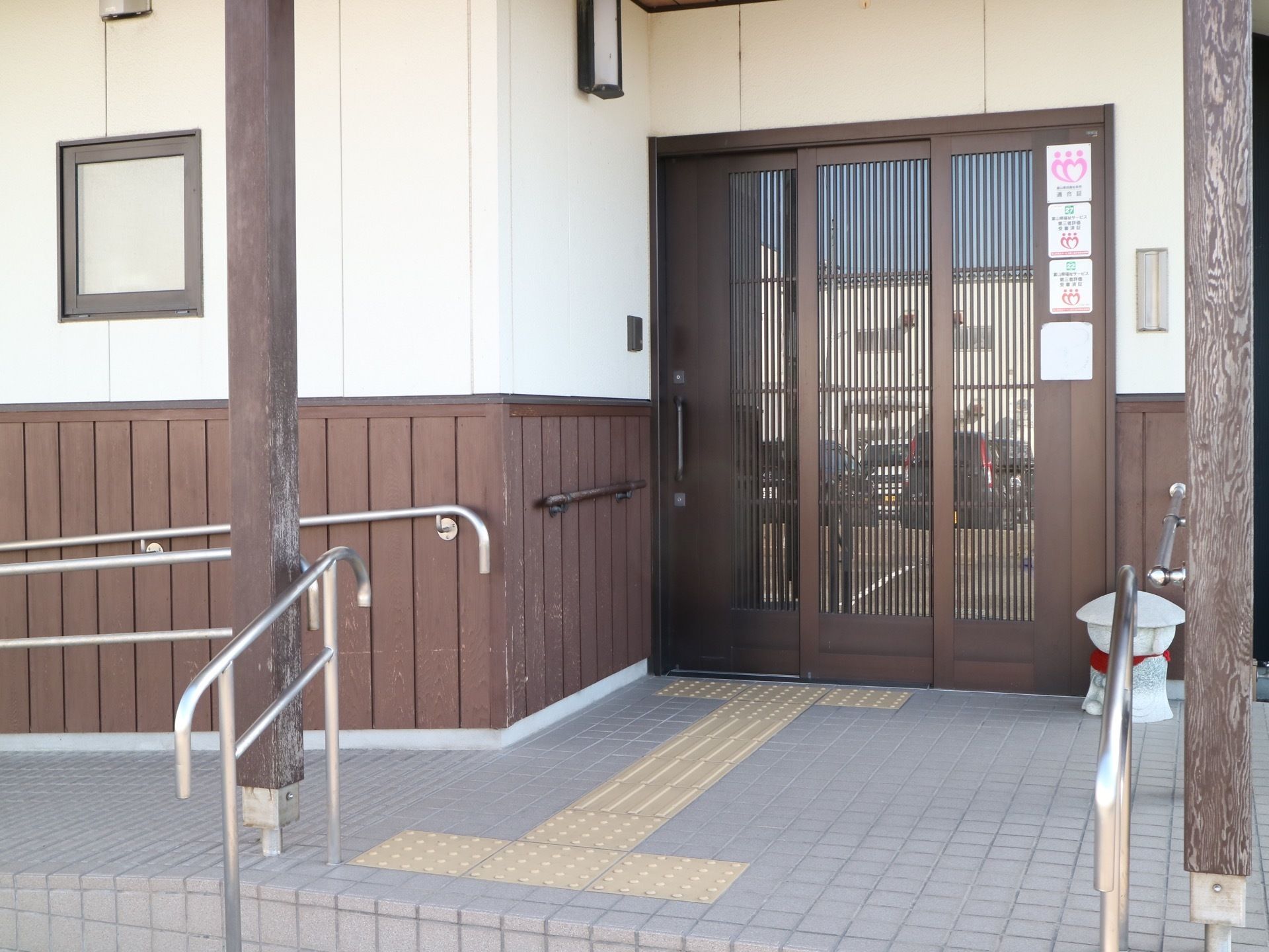 正面奥に３枚の引き戸でできた玄関が見えている。地面には視覚障害者用の点字ブロックが貼り付けられている。