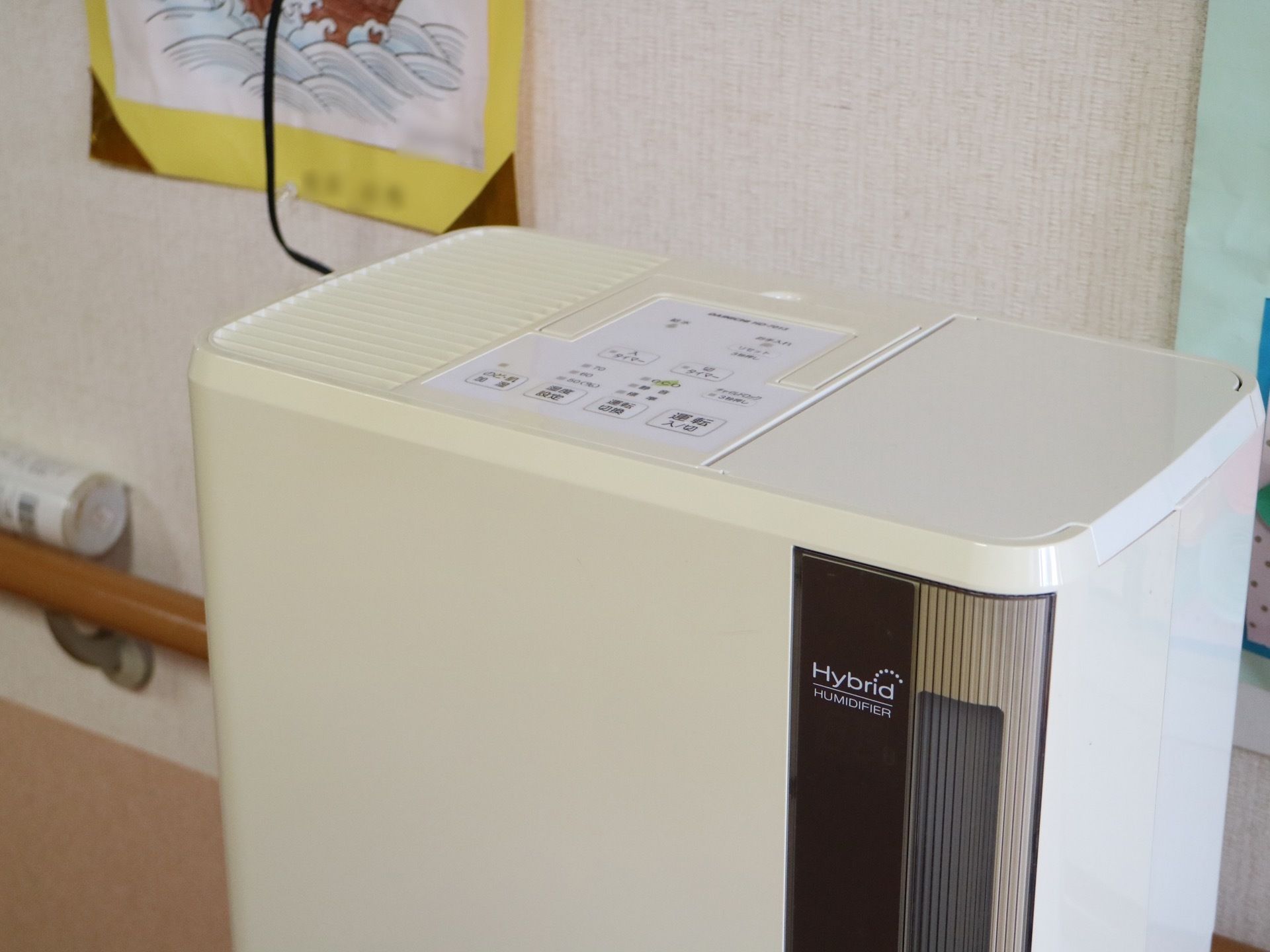 白い壁に、掲示物が貼られ、木製の手すりが取り付けられている。手すりの上には、筒状のものが置かれている。