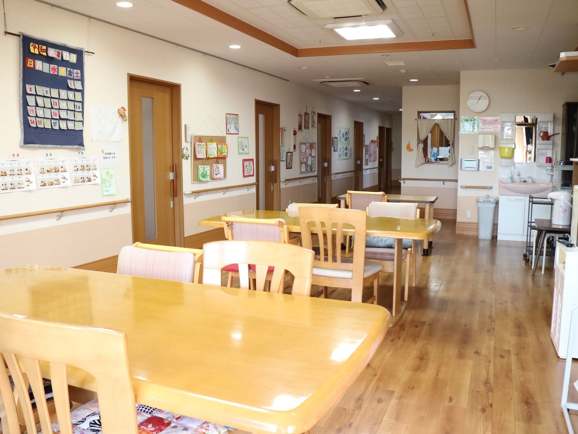 通路との間に壁がない空間に、テーブルと椅子が並べて置かれている。通路の壁には、たくさんの掲示物が貼ってある。