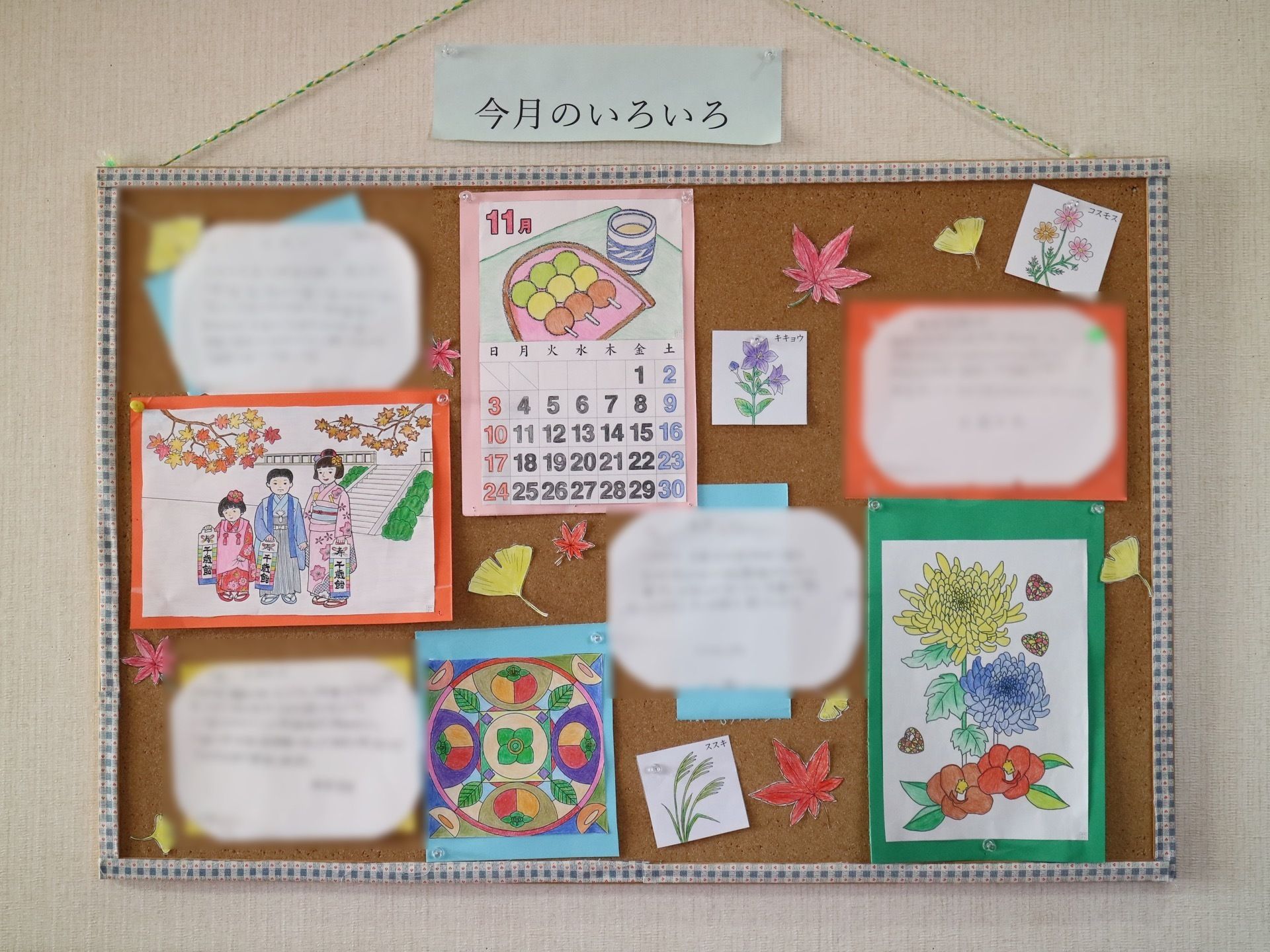 白い壁に掲示物がかけられている。チェック柄の枠の板に、季節の草花や行事などを手作りしたものが貼ってある。