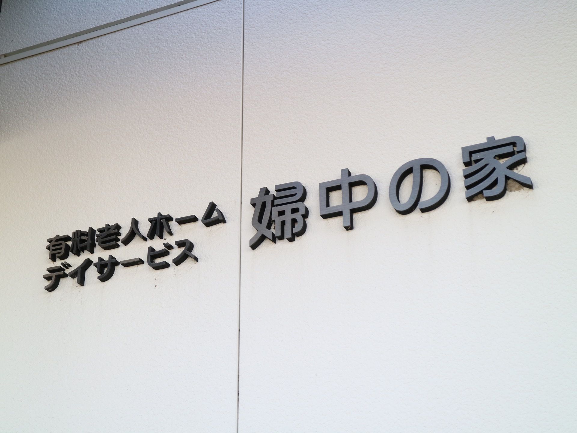 白い継ぎ目のある壁に、施設名が取り付けられている。施設名は黒色で、1文字ずつ独立した文字となっている。