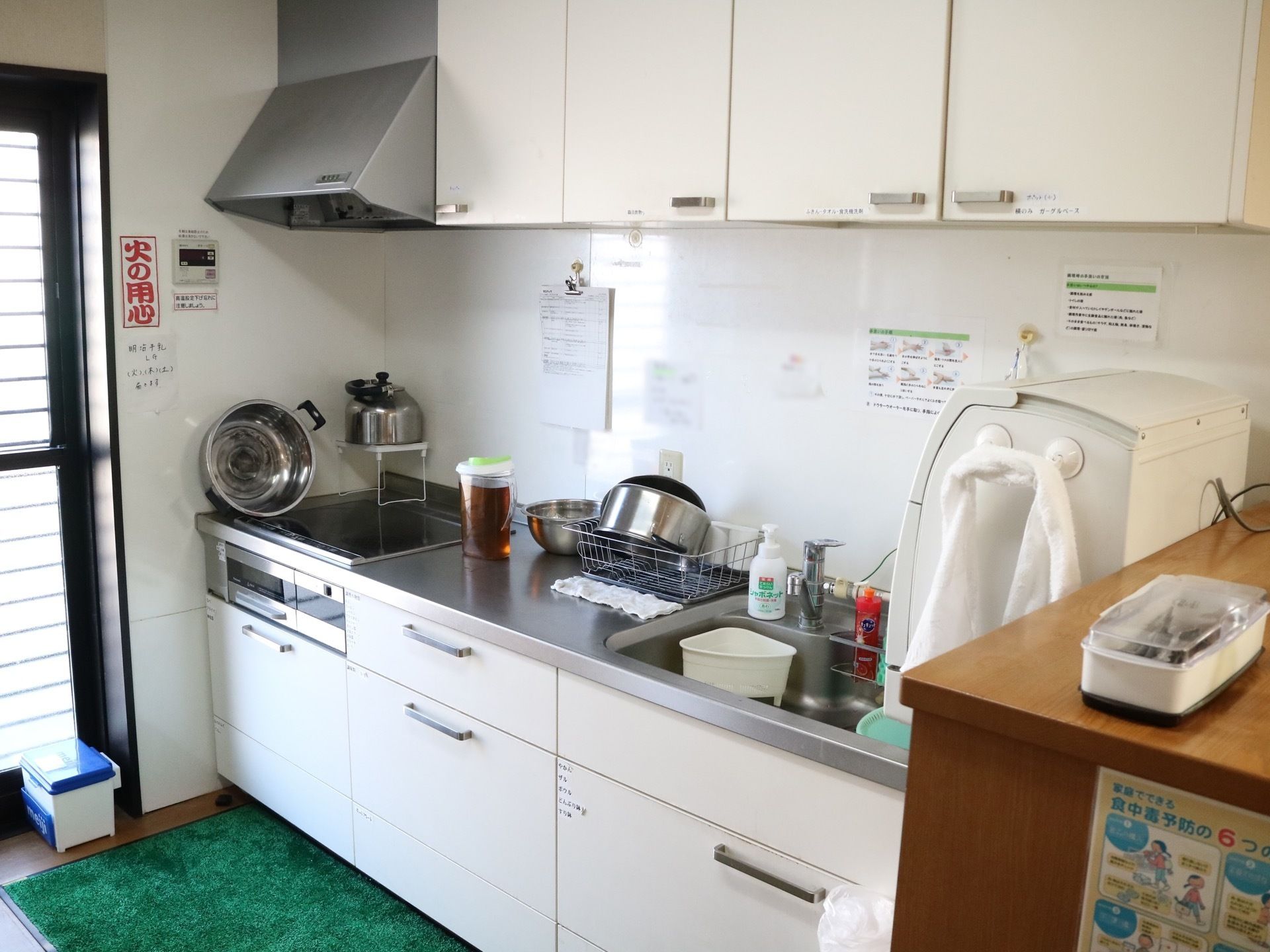 白を基調としたキッチンである。IHコンロが設置され、銀色の鍋が立て掛けてある。端には、勝手口の扉が見える。