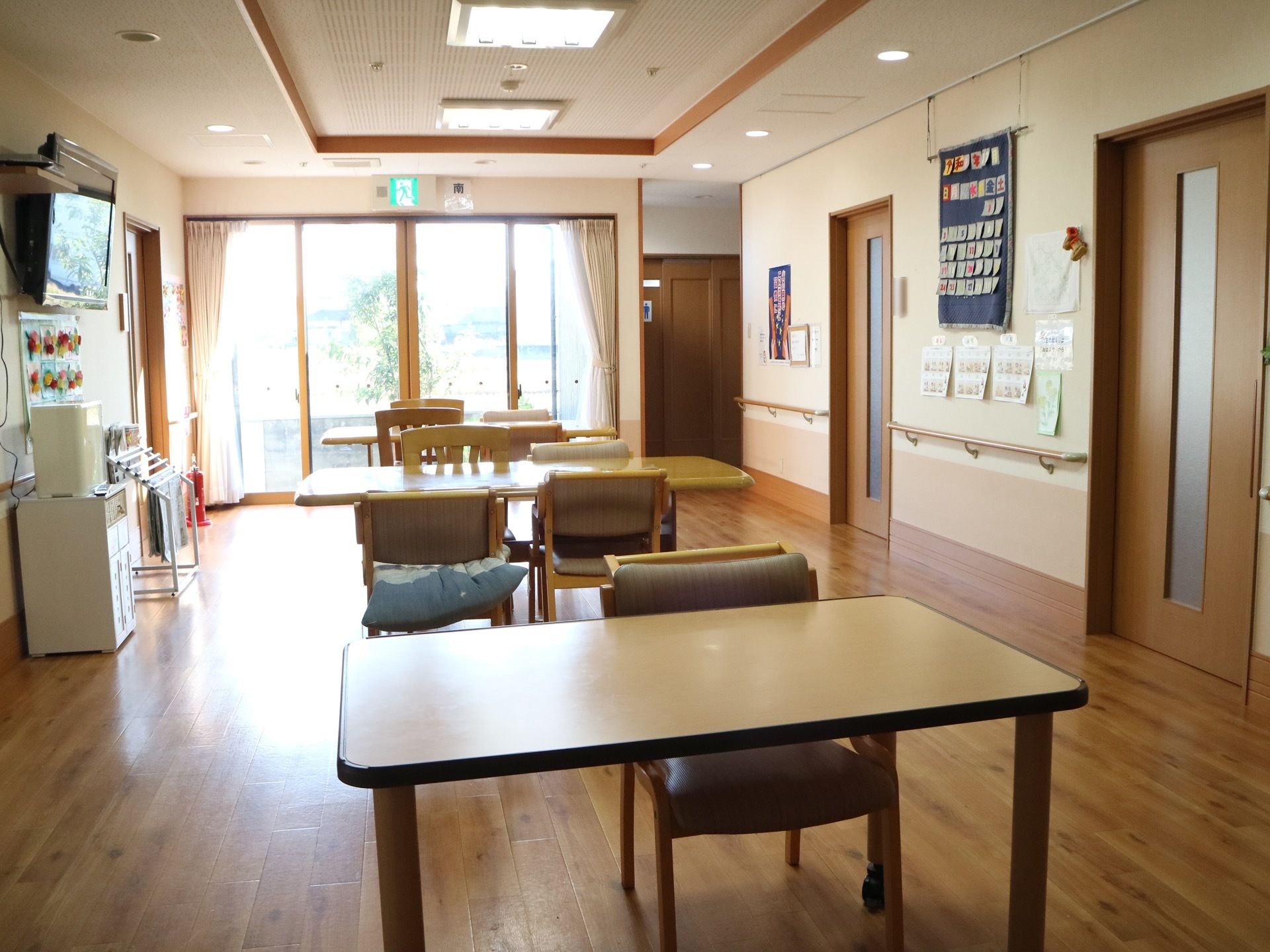 奥に、大きな窓が4枚並んでいる。窓からは外の景色が見える。また、壁には壁掛けのテレビが設置されている。