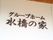 白い外壁に取り付けられた施設名の図である。屋根があるところの壁に、漆喰に黒い塗料が塗られた看板が付いている。