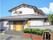 建物は瓦屋根の2階建てで、玄関扉は引き戸になっている。アプローチの階段には手すりが設置され、塀づたいに植え込みがある。