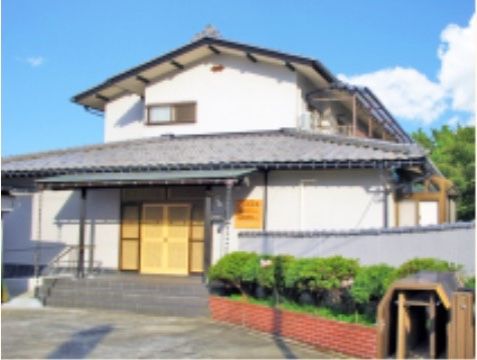 民家風の建物2階にベランダがあり、玄関には大きめのひさしが設置されている。アプローチにはタイルが敷かれ、サイドに手すりが付いている。