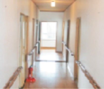 床が木目調の廊下には、消火器が1台置かれている。壁には手すりが付いており、廊下の両側には部屋の扉が並んでいる。