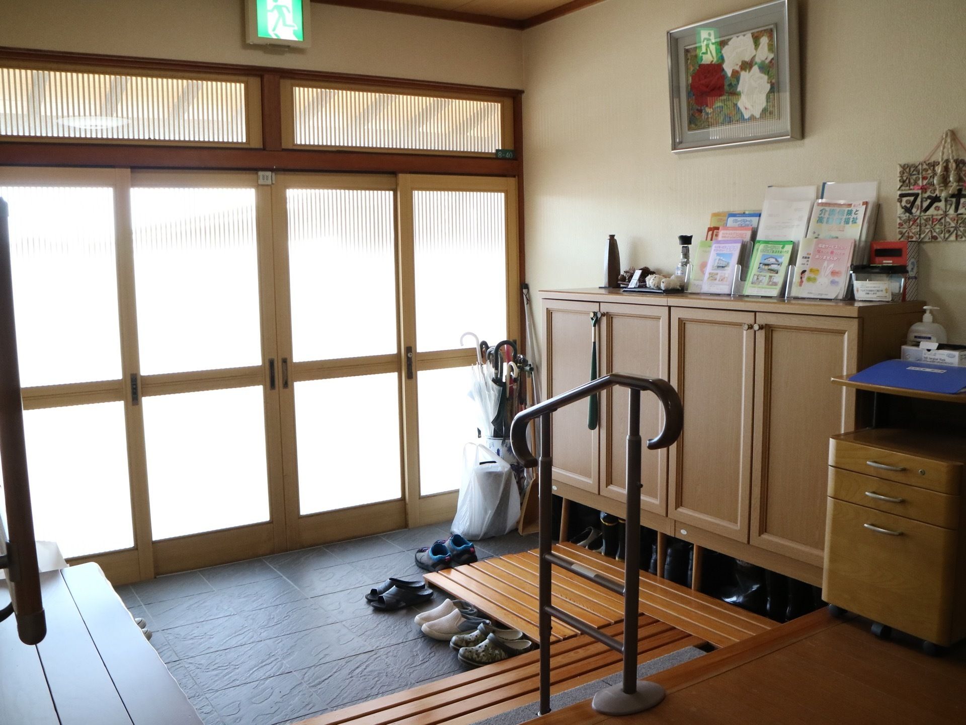 昔の一般住宅のような間口の広い玄関で、壁際に下駄箱、その横に傘立てがあり、地面にはすのこが置かれている。