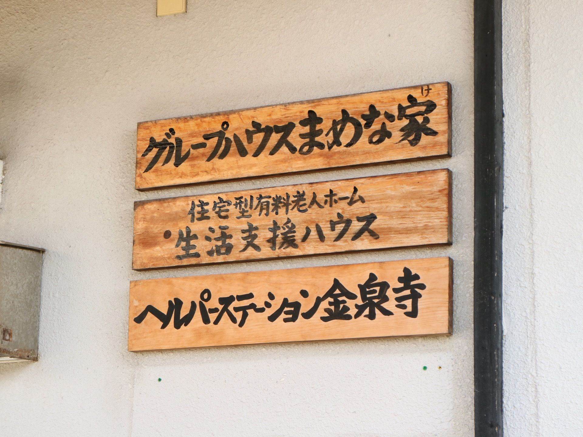 施設玄関横に木製の看板が掛けられており、施設名が書かれている。掛けられてから年月が経っているせいか、味が出ている。
