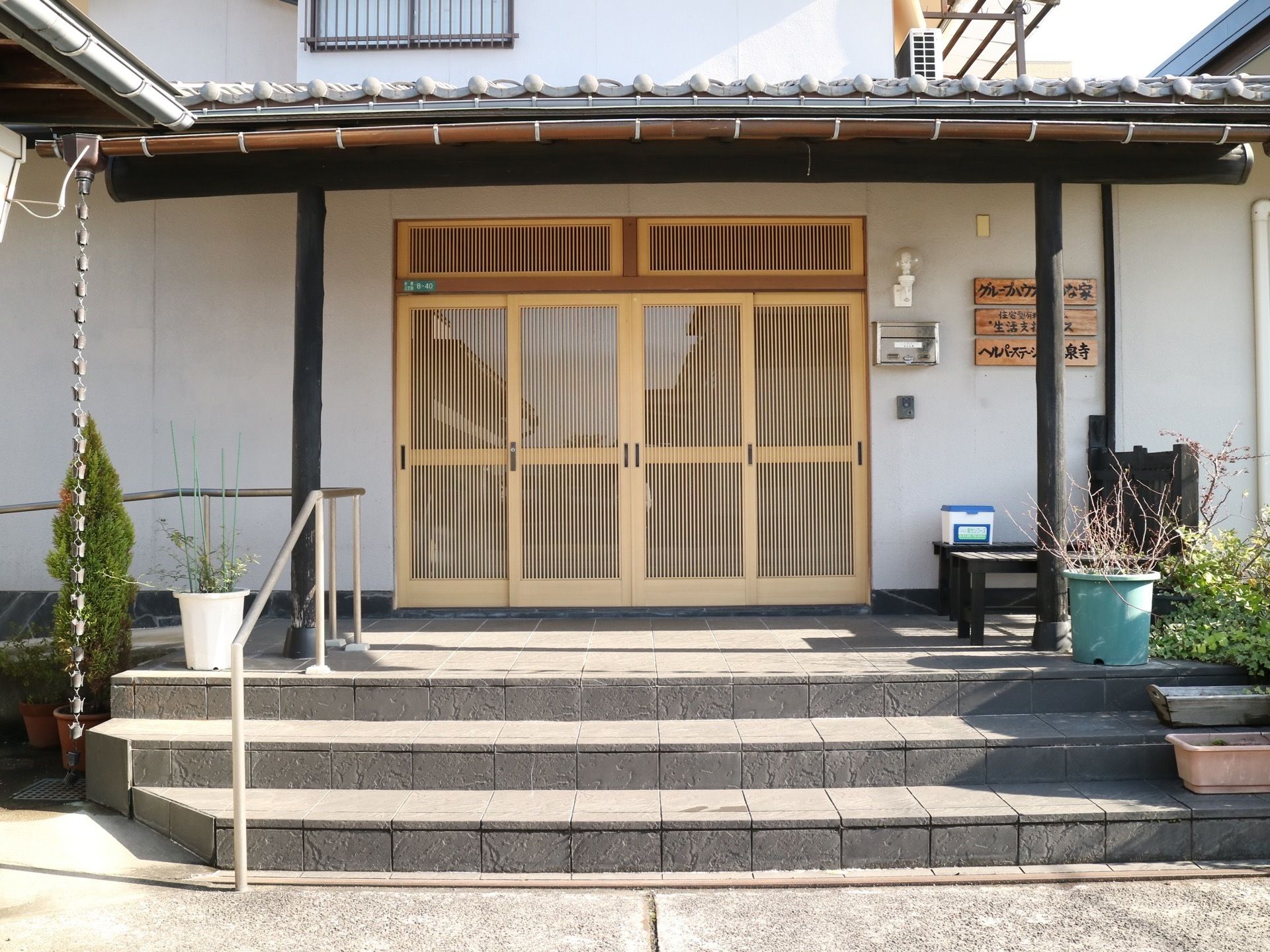 石造りの階段を中心に複数の植木鉢が並び、日本家屋らしい雰囲気を感じさせる玄関である。脇にはスロープがあり、手すりも設置されている。