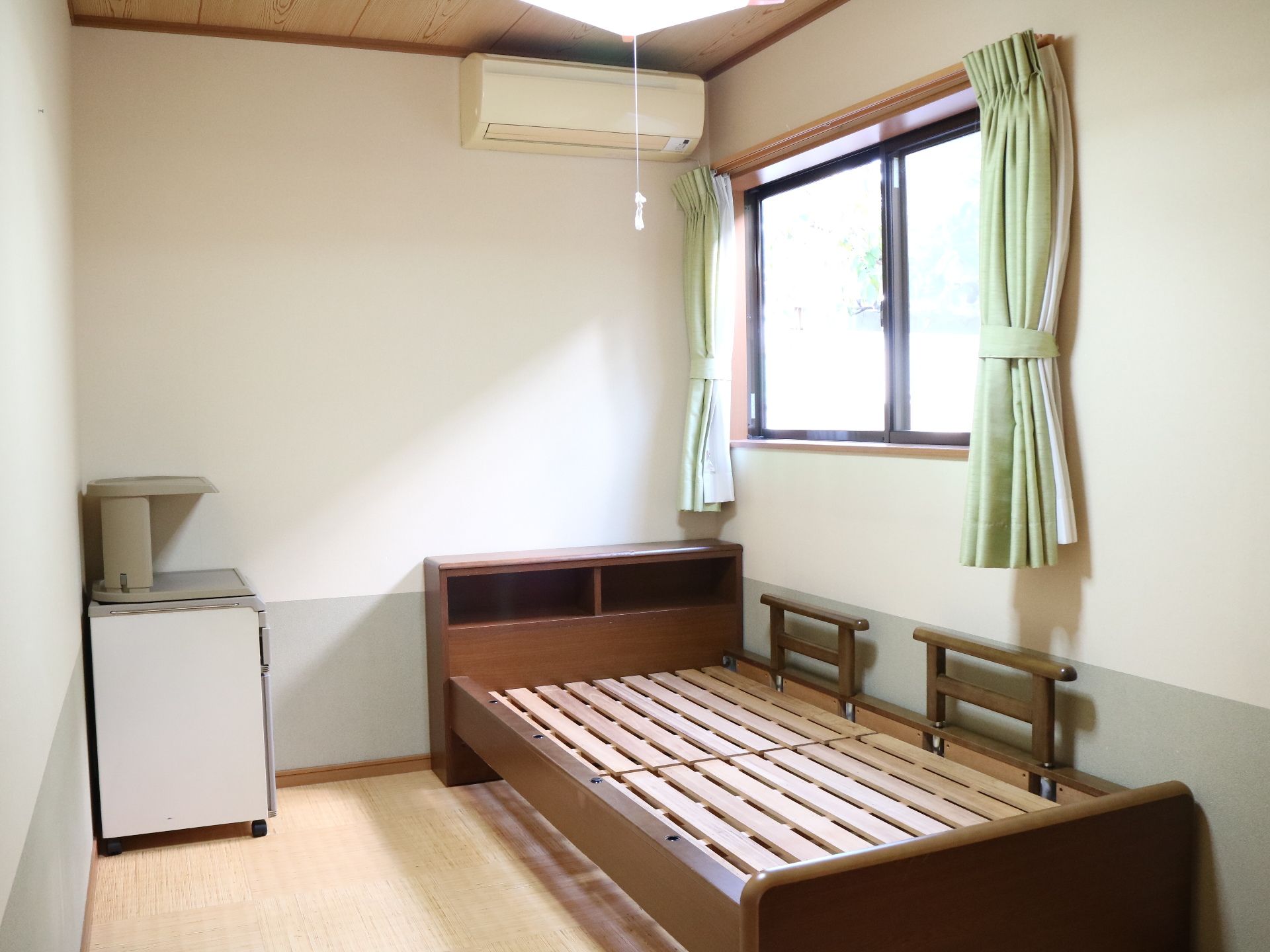窓の下に設置されている、マットレスが置かれていないベッド