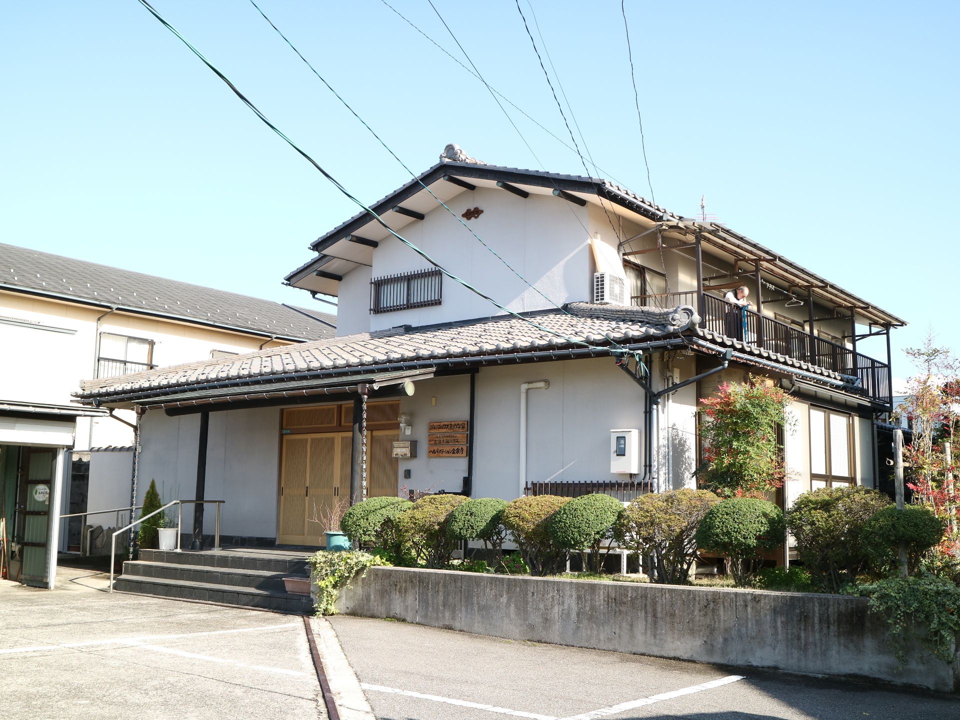 瓦屋根の和風一軒家のような施設の手前に、丸く剪定された垣根