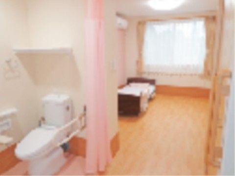 エアコンが完備された居室の奥に、介護ベッドが設置されている。大きな窓にはレースとカーテンが取り付けられている。