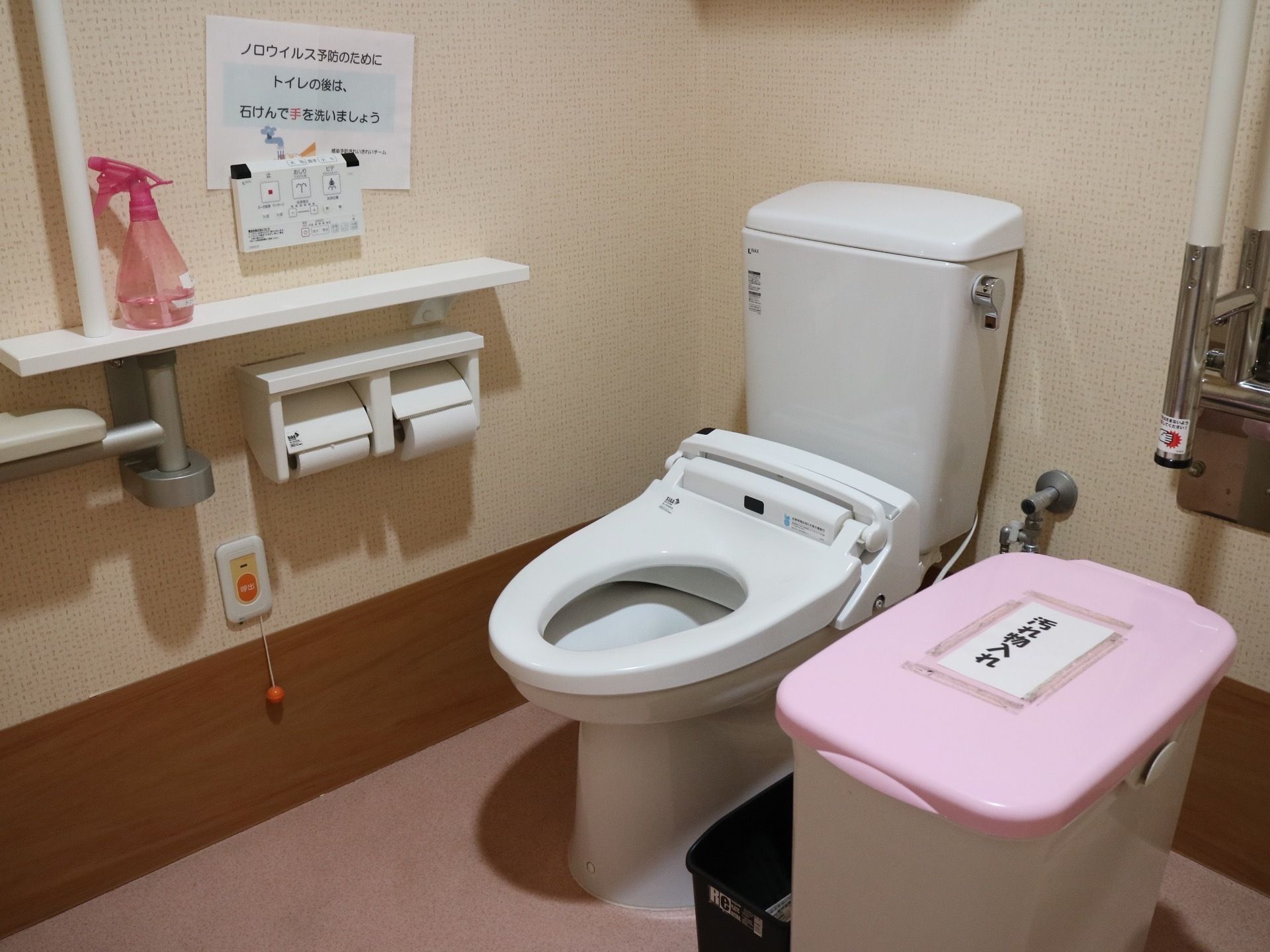 広いスペースにトイレが設置されている。便器のすぐ横に、ピンク色のふたがついた汚物入れが置かれている。